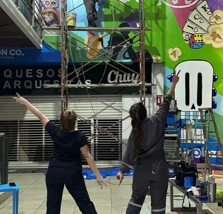 Cristina y Karina pintando un mural sobre andamio